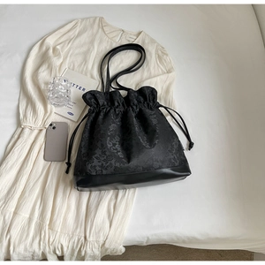 Macro detail of black floral jacquard tote bag with drawstring closure and leather bottom