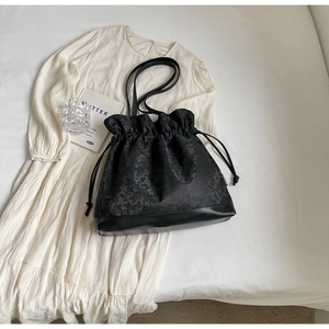 Detail of black jacquard drawstring tote with textured floral pattern and leather bottom