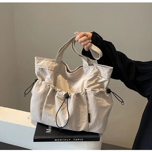 Close-up of beige pleated tote bag featuring functional black drawstring outer pockets