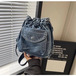 Detail der blauen Denim-Beuteltasche mit Kordelzug, Silberknopf und vorderer Klappentasche