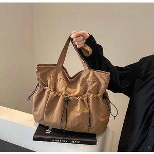 Detail of khaki pleated tote bag featuring external drawstring pockets and nylon texture