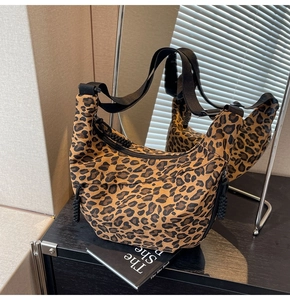 Close-up of leopard print dumpling bag with black wide strap and woven zipper pull detail