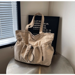 Detail of beige pleated tote bag with multiple drawstring pockets and smooth nylon texture