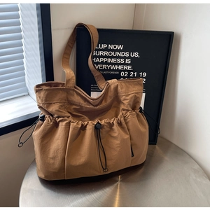 Brown nylon pleated tote bag with drawstring outer pocket on a metal table