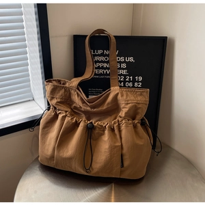 Detail of brown pleated tote bag featuring drawstring accents and functional buckles