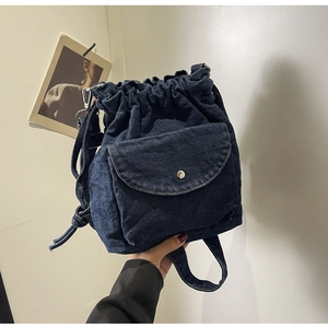 Detail eines dunkelblauen Denim-Rucksacks mit Kordelzug, Klapptasche und Metallschnalle