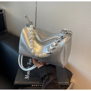 Détail du sac cylindrique argenté avec anse en perles et chaîne cœur sur un livre