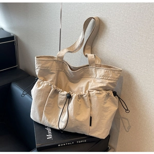 Detail of beige pleated tote bag showing drawstring pocket and logo label on side