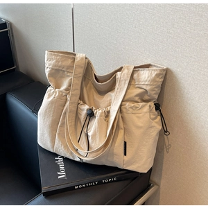 Close-up of pleated nylon tote bag featuring a side drawstring pocket and black woven label
