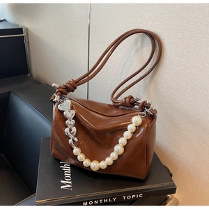 Détail d'un sac cylindrique marron avec perles blanches et breloques coeur argent