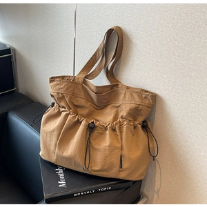 Detailed close-up of brown nylon tote bag featuring drawstring pockets and long handles