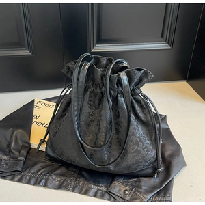 Detailed close-up of the black floral jacquard fabric and leather strap on a drawstring bag