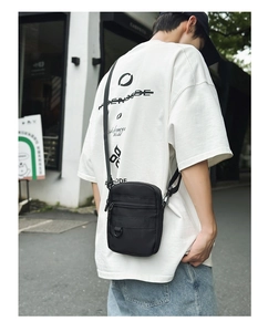Outdoor street view of a man wearing a black waterproof nylon crossbody messenger bag