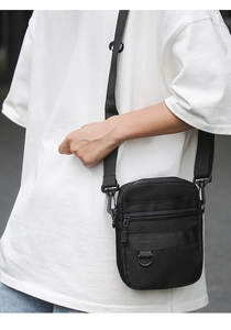 Close-up of black nylon crossbody bag with adjustable strap and metallic D-ring on model