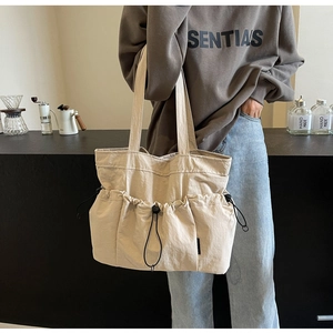 Detail of the pleated beige tote bag with side drawstrings in a lifestyle café setting