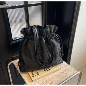 Detail of black drawstring bucket tote with jacquard texture and smooth leather strap