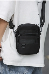 Close-up of black crossbody bag detail showing front zipper pocket and metal D-ring