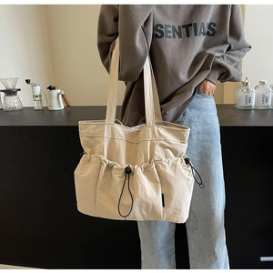 Detail of beige pleated tote bag with drawstring pockets and adjustable black buckles