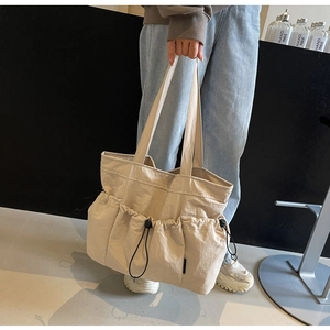 Detail of off-white canvas tote bag featuring functional drawstring exterior pockets
