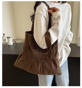 Detail of a large brown canvas tote bag featuring unique pleated design and contrast stitching