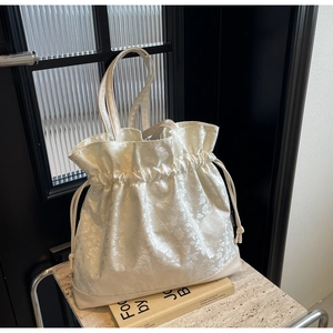 Detail of cream drawstring tote bag featuring jacquard floral texture and slim handles