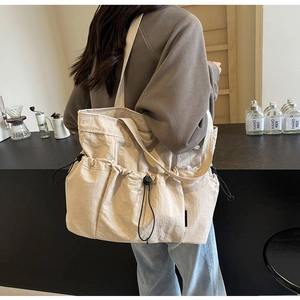 Detail of beige pleated tote bag with drawstring pockets in a cafe setting