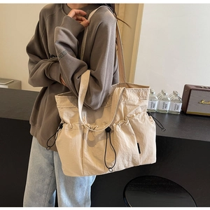 Detail view of a beige drawstring tote bag with pleated side pockets and wide shoulder strap