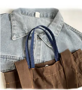Detail of brown canvas tote bag with denim handles and decorative yellow stitching
