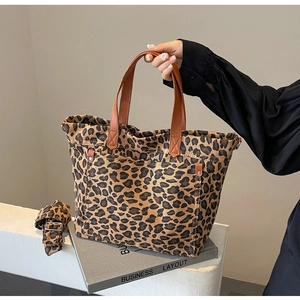 Detail of leopard print canvas tote bag featuring brown leather handles and side pocket