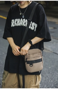 Detail of khaki crossbody bag with front zipper pocket and black utility D-ring strap