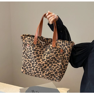 Detail of leopard print canvas tote bag featuring brown leather handles and outer pocket