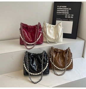 Close-up of bucket bags with quilted texture, pearl straps, and metal chains on marble