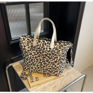 Detailed leopard print canvas tote bag with leather handles on marble display stand