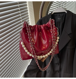 Detail of burgundy quilted bag with pearl strap and chain against a black suit
