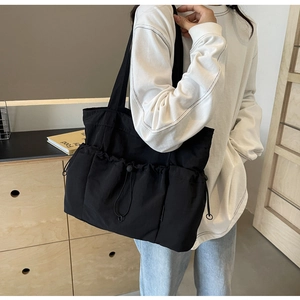 Detail of black pleated nylon tote bag with drawstring pocket shown on shoulder