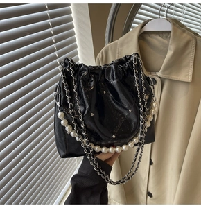 Detail of black pleated patent leather bag with large pearl handle and silver chain strap