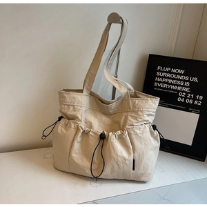 Detail view of beige pleated tote bag with drawstring closure and functional pockets