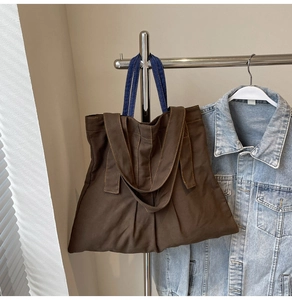 Detail view of brown canvas tote with dual-tone blue handles and visible yellow stitching