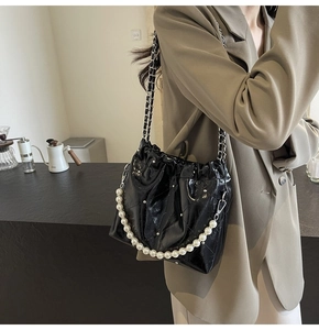 Detail of black quilted shoulder bag with pearl handle and silver chain on model