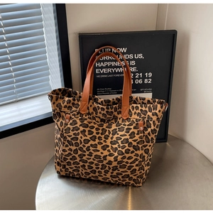 Detail of leopard print canvas tote bag featuring brown leather handles and rivets