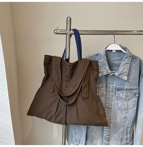 Detail of canvas tote bag showing dark brown fabric, blue handles, and side pleat design