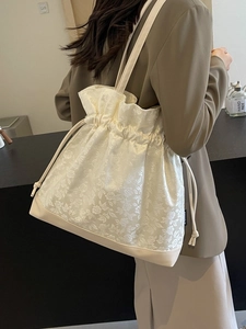 Minimalist cream drawstring tote bag with floral jacquard texture and slender shoulder strap