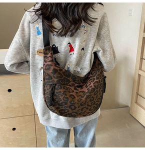 Detail of leopard print crescent bag with black wide strap and textured canvas fabric