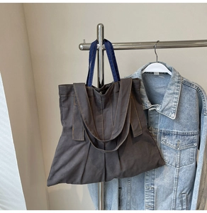 Detail of grey canvas tote bag with yellow stitching and blue denim handles on hook