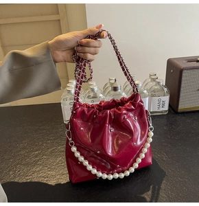 Detail of red quilted bucket bag with shiny faux leather and elegant pearl chain
