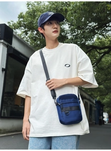 Outdoor street view of a navy blue nylon crossbody bag with multi-layer zippers