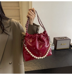Detail of red quilted patent leather handbag with silver studs and pearl chain strap