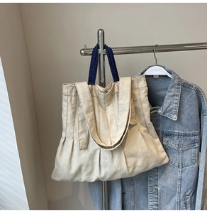 Detail of canvas tote bag with textured pleats, denim handles and metal snap closure