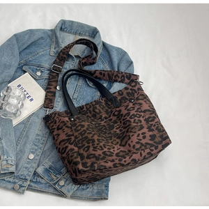 Detailed leopard print tote bag with black handles and adjustable shoulder strap over denim