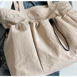 Detail of beige pleated tote bag with dual drawstring pockets and textured nylon fabric